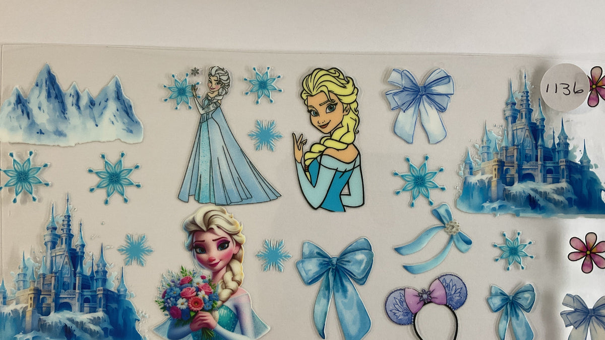 A sheet of Elsa-themed sticker decals featuring illustrations of Princess Elsa, blue snowflakes, icy mountains, a castle, and blue bows on a white backing.